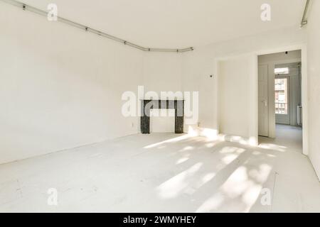 An empty white room featuring a classic black marble fireplace and natural sunlight casting shadows on the floor. Stock Photo