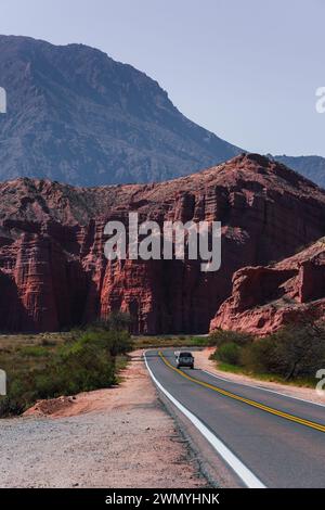 Car driving on a road curving through the towering red cliffs of Los Castillos with a backdrop of a mountain and clear skies Stock Photo