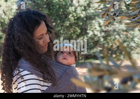 A tender moment between a mother with curly hair and her baby boy wearing a cap, wrapped in a blanket outdoors Stock Photo