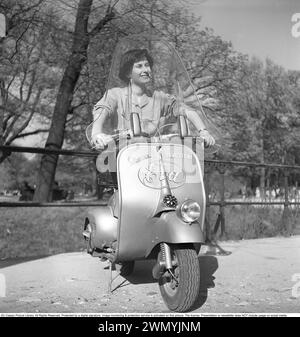 Driving in Italy in the 1950s. A young woman on a Vespa scooter in Milan Italy 1950. The manufacturer Piaggios biggest sales promo ever was Hollywood. In 1952, Audrey Hepburn side-saddled Gregory Peck's Vespa in the feature film Roman Holiday for a ride through Rome, resulting in over 100,000 sales.  Kristoffersson Ref AY28-1 Stock Photo