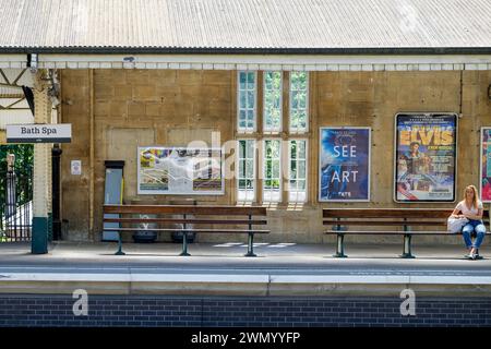 A woman is pictured on a platform sitting on a seat waiting for a train at Bath spa train / railway station station. Stock Photo