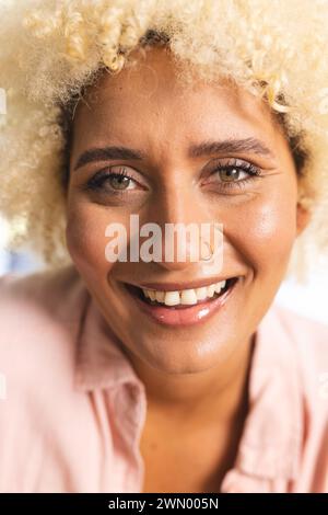 Young biracial woman smiles warmly on a hike, her curly hair framing ...