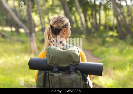 Young woman with a backpack stands amidst greenery on a hike Stock Photo