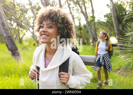 Young biracial woman with curly hair smiles while on a hike, friend in background Stock Photo