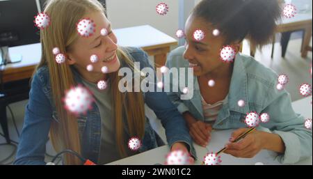 Image of Covid 19 coronavirus cells spreading over two female students working together Stock Photo