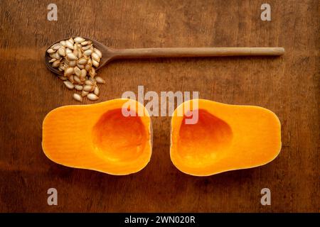 Two halves of sliced ripe butternut squash with seeds and vintage wooden spoon on rustic wooden tabletop from above Stock Photo