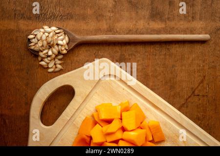 Pieces of cut butternut squash and vintage spoon on rustic wooden tabletop from above Stock Photo