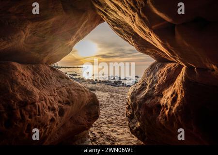 Within the depths of Veczemju Klintis Cave, twilight descends like a gentle melody, enveloping the rocky beach in a surreal tapestry of sunset magic. Stock Photo