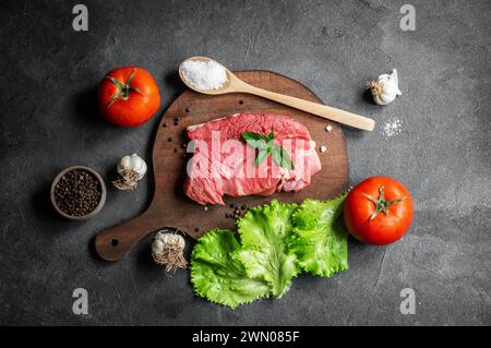 Raw beef steak meat on cutting board on rustic background with mint leaves, peppers and lettuce, butcher concept Stock Photo