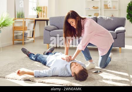 Young woman doing CPR on unconscious man lying on the floor at home. Stock Photo