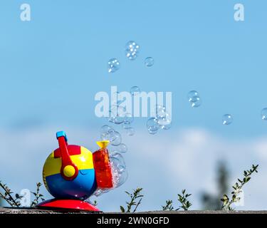 Colourful bubble-blowing toy releasing soap bubbles against a bright blue sky, playful outdoor still life with copy space.. Stock Photo