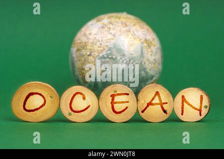 Ecological concept. On a green background there is an Earth globe and wooden roundels with the inscription - Ocean Stock Photo
