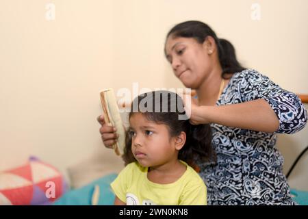 A warm scene of a mother gently combing her daughter's hair, creating a loving connection in their cozy bedroom Stock Photo