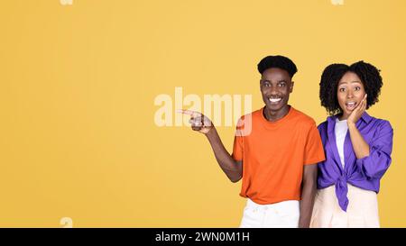 An animated young man in an orange shirt points to the side while a surprised young woman Stock Photo