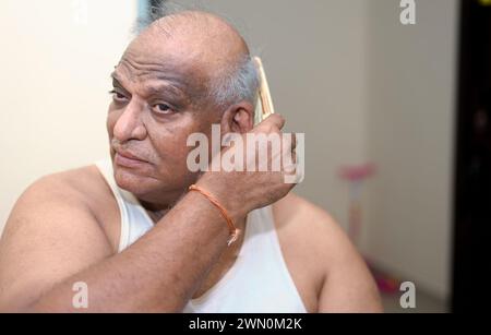 A close-up photo of a confident bald senior man using a well-worn wooden comb to style his hair Stock Photo