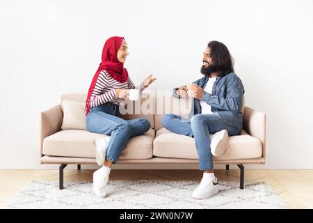 Cheerful Young Muslim Couple Resting Together At Home, Drinking Coffee And Chatting Stock Photo