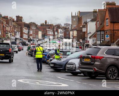 Traffic wardens patrol busy street in historic town of Marlborough Wiltshire, lined with cars and traditional architecture. Stock Photo