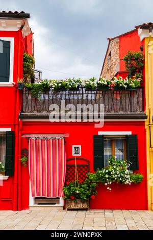 Bright traditional red house on Burano island, Venice, Italy. Colorful curtain on door, wooden old style windows with shutters and Mandevilla flowers Stock Photo