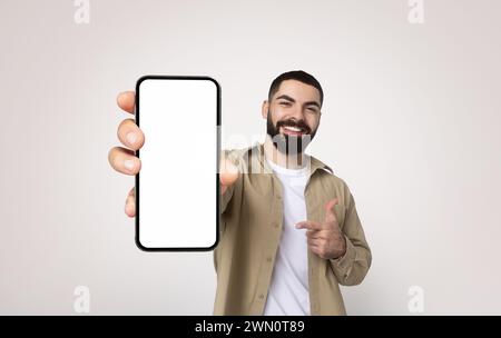 Joyful bearded man in a casual khaki shirt and white t-shirt smiling and pointing at a smartphone Stock Photo