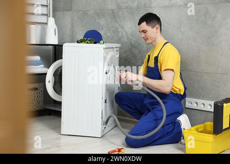 Young plumber examining drain hose of washing machine in bathroom Stock Photo
