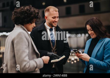 Three people in stylish winter attire share a moment of joy looking at a smart phone on a city street, exuding teamwork and connectivity. Stock Photo