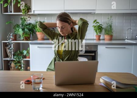Overworked woman freelancer sitting at table with eyes closed, resting after long hard job on laptop Stock Photo
