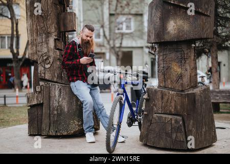 Hipster man checking his smart phone leaning on a bike in the city Stock Photo