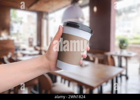 Coffee paper cup held in hand with coffee shop in the background. Space for logo promotion Stock Photo