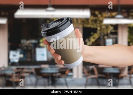 Logo mockup on a paper takeaway cup held in hand in front of a coffee shop Stock Photo