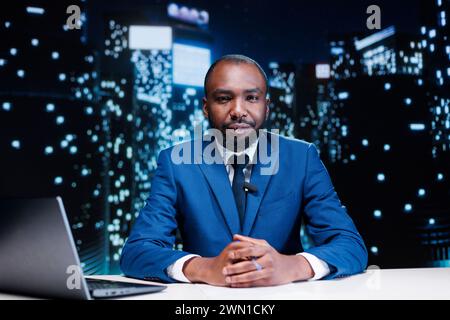 Anchorman hosting night show live on television network, discussing about important information and latest events. African american presenter working in tv broadcast and media industry. Stock Photo