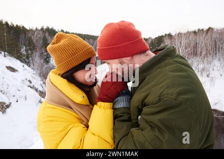 Side view shot of Caucasian couple having date in mountains on winter day, man kissing his girlfriends hand Stock Photo
