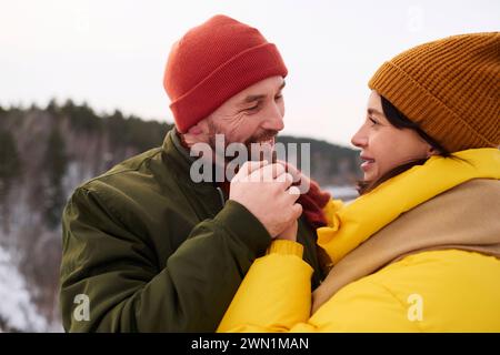 Medium closeup of happy bearded Caucasian man holding hands of his wife while standing outdoors on cold winter day Stock Photo
