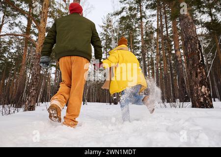 Rear view shot of unrecognizable young man and woman in love having fun running along forest park on winter day Stock Photo