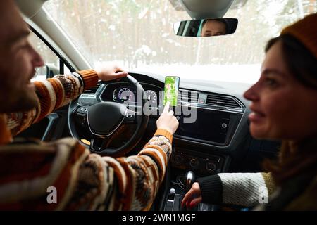 Selective focus shot of man using navigation app on smartphone and talking to his wife while driving car on winter day Stock Photo
