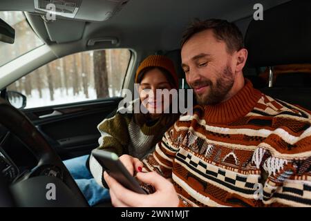 Cheerful Caucasian couple sitting in car reading map on smartphone Stock Photo