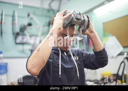 Portrait of an hispanic young worker removing a respiratory protection mask, as he finishes a spray painting job in his workshop. Health protection in Stock Photo