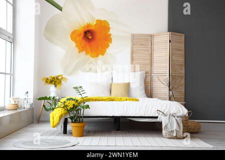 Stylish interior of bedroom with beautiful narcissus flower on wall Stock Photo