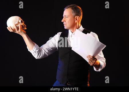 Mature actor with skull reading script on dark background Stock Photo