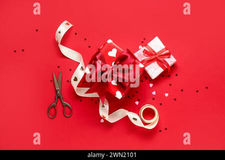 Beautiful gift boxes with ribbon, scissors and confetti on red background. Valentines Day celebration Stock Photo