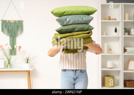 Woman holding stack of pillows with folded warm plaid in room Stock Photo