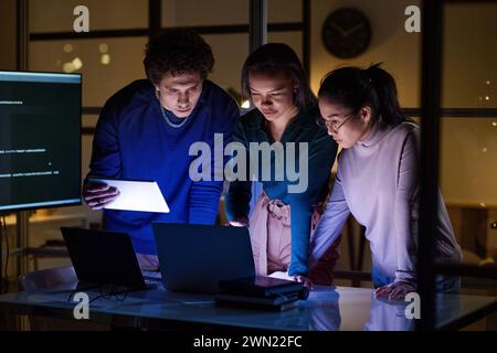 Three ethnically diverse programmers working on new software in IT company office at night Stock Photo