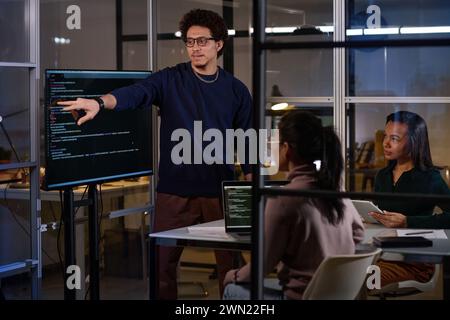 Group of three young ethnically diverse IT specialists working together on code in office late in evening Stock Photo