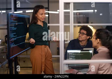Ethnically diverse programmers working together on code at workplace in IT company office late in evening Stock Photo