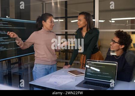 Group of three young ethnically diverse programmers working together on code in office late in evening Stock Photo