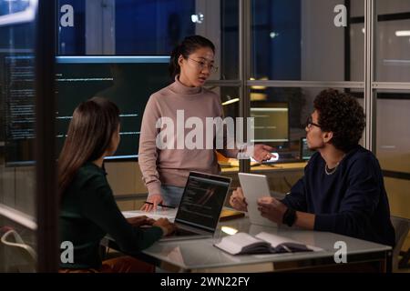 Group of ethnically diverse programmers spending evening in office working together on computer code Stock Photo