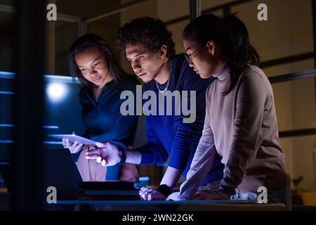 Group of modern young IT specialists developing and testing new software late in evening Stock Photo