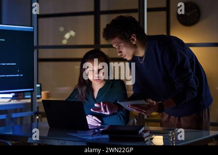 Ethnically diverse young male and female programmers working together on code in IT company office at night Stock Photo