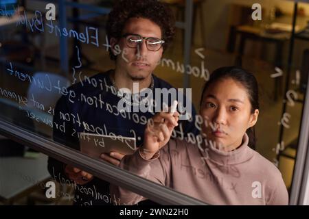 High angle of two young programmers working together on code writing it on glass wall in modern office Stock Photo