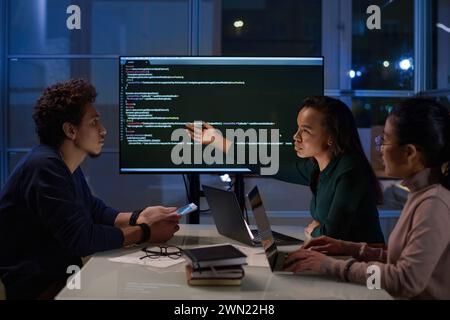 Group of three young ethnically diverse programmers working together on code in office at night Stock Photo