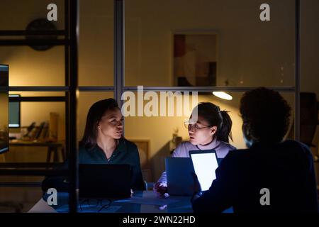 Ethnically diverse man and women working together in office late in evening discussing project Stock Photo